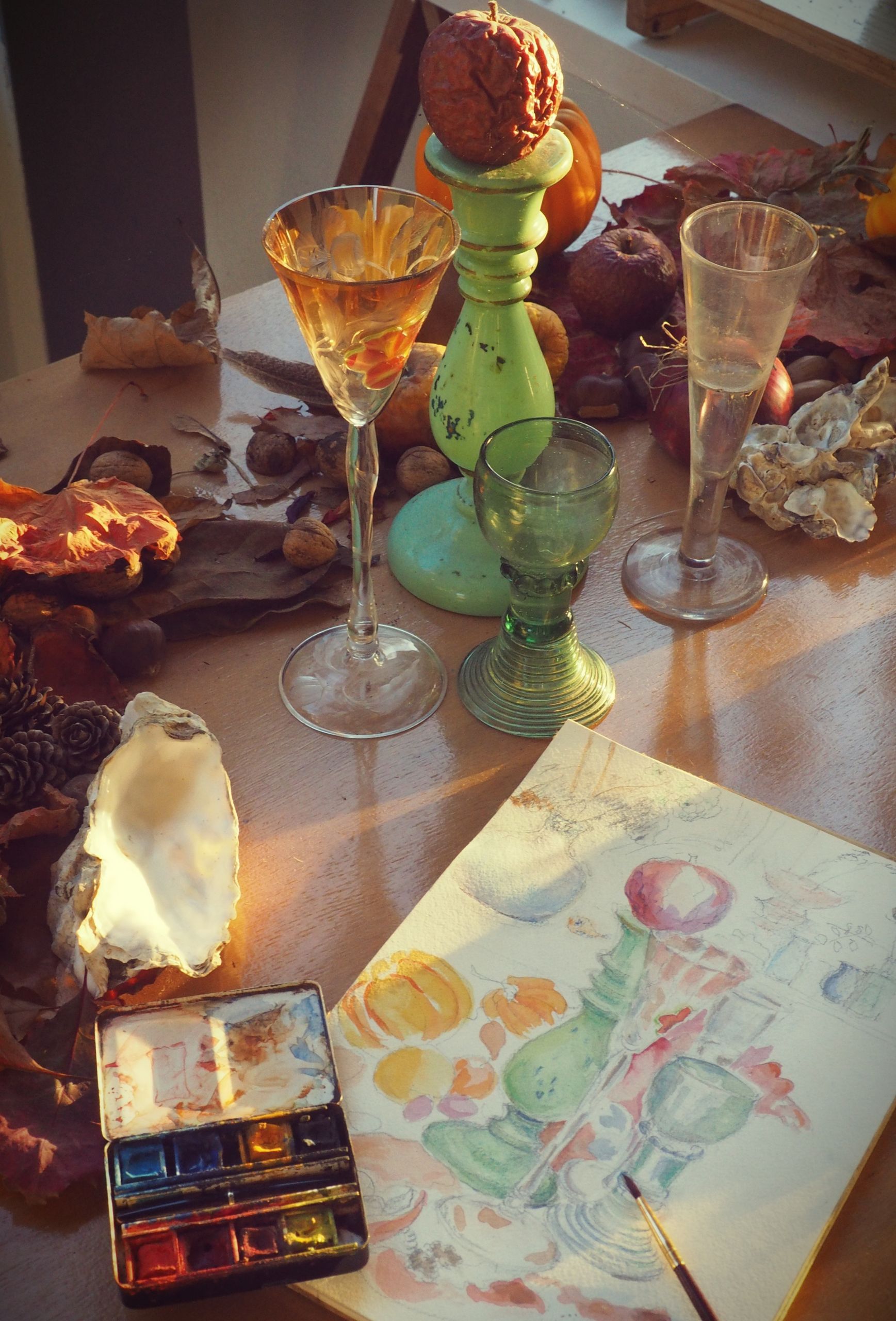 A beautifully crafted still life featuring glassware, paintings, and autumn accents in warm sunlight.