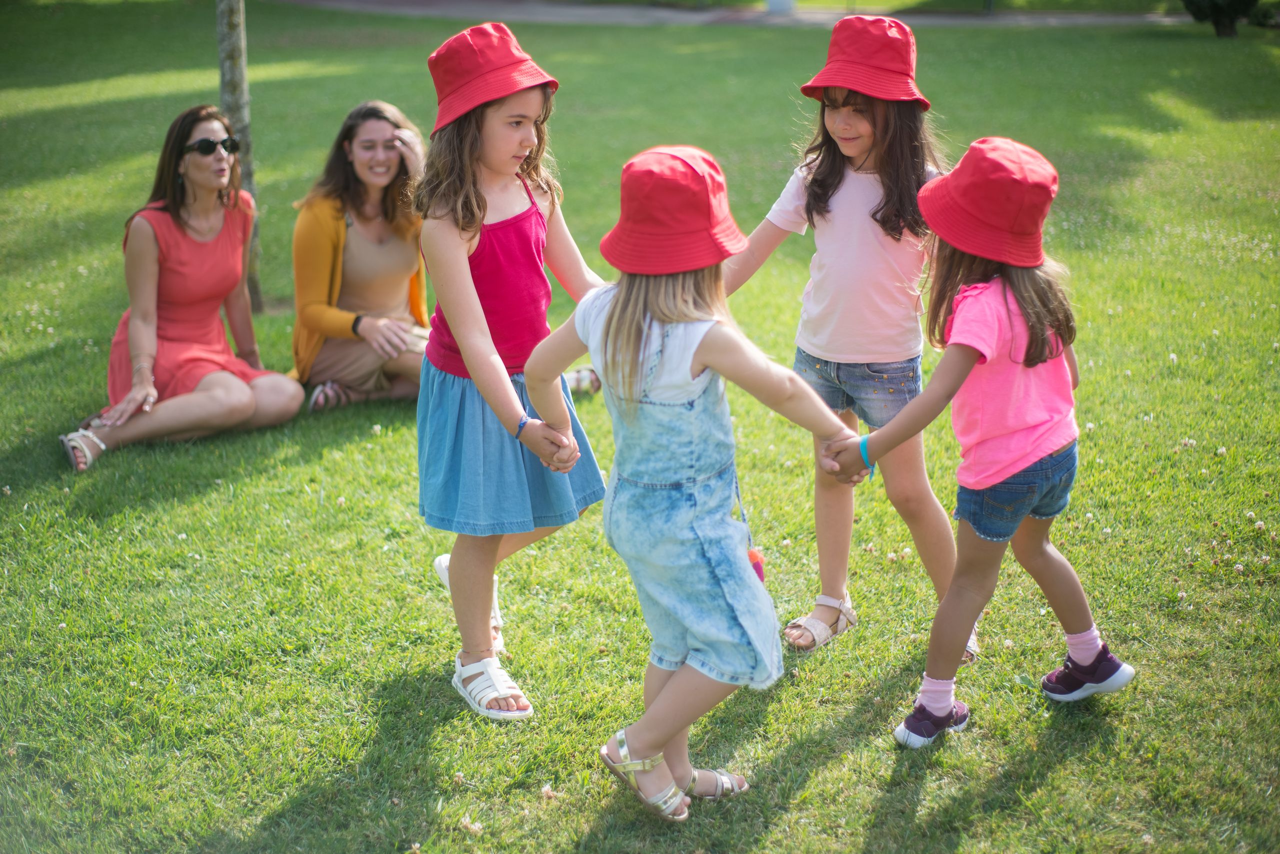 Five children in red hats playing in a sunny park in Portugal.