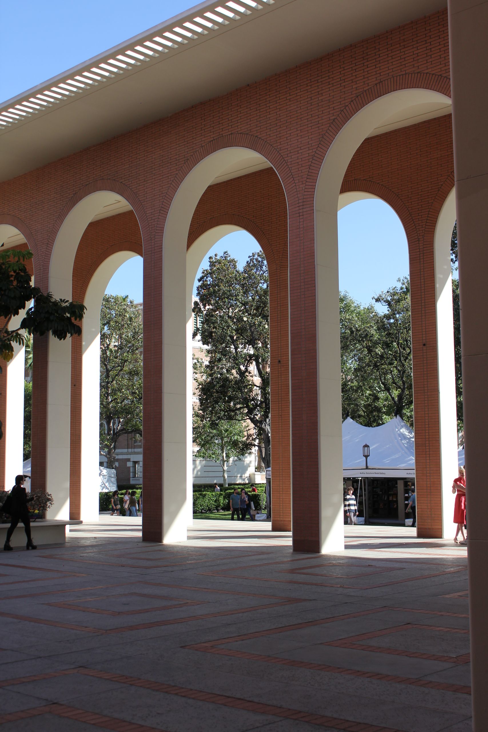 View of brick and concrete arches on a university campus with trees and outdoor structures.